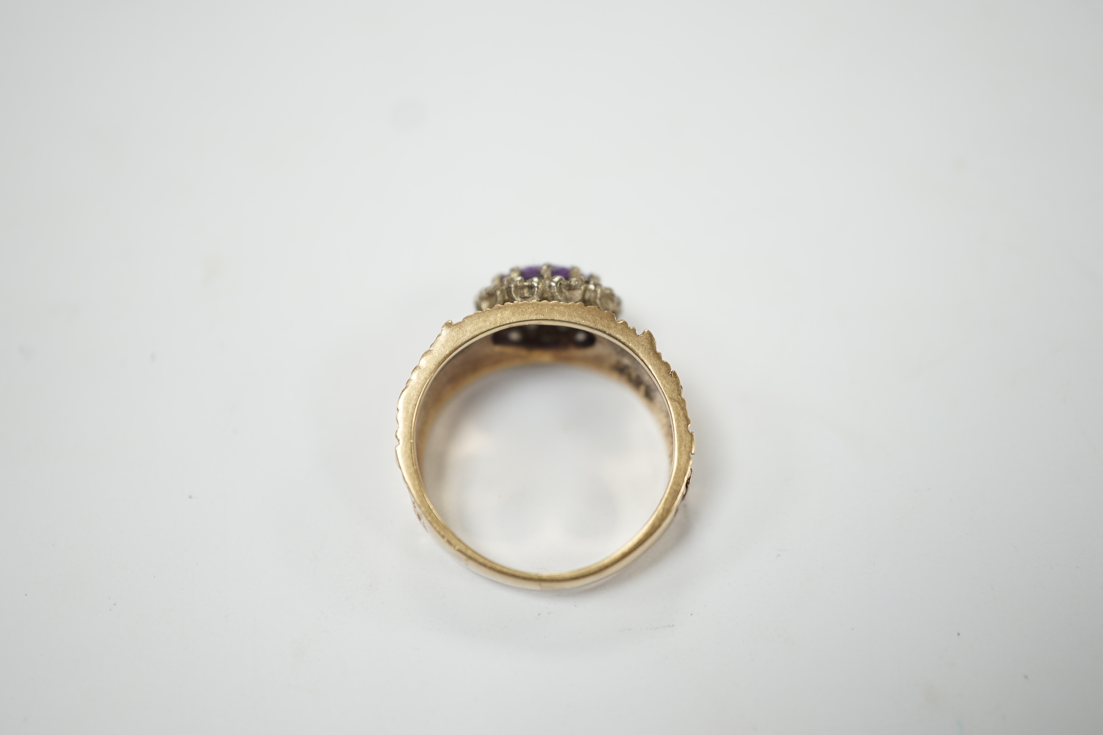 A textured yellow metal, amethyst and simulated diamond set oval cluster ring, size M, gross weight 4.4 grams. Fair condition